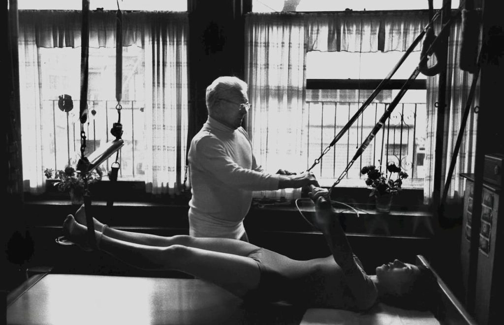 Joseph Pilates pomaže devojci na reformeru i daje joj instrukcija kako pravilno da radi pilates vežbe.